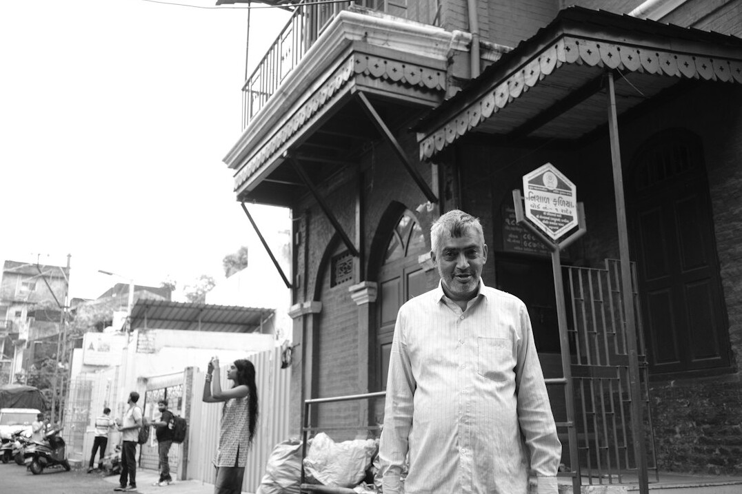 Portrait of a South Asian man in his early forties beside a broadcast camera